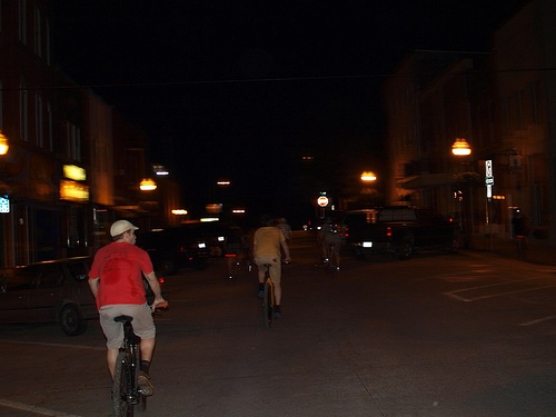 Rear view of cyclists, riding their bikes down a town street at night, with lights and buildings on the sides